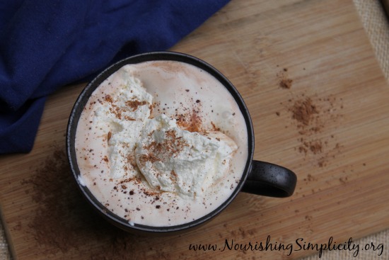 Brown mug with steaming hot cocoa topped with whipped cream and sprinkled with cocoa powder