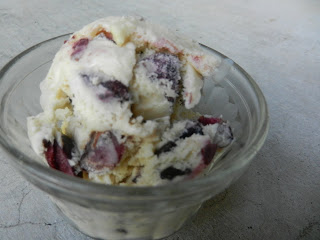 Small clear glass bowl with a small scoop of vanilla ice cream with chocolate and cherry pieces. 